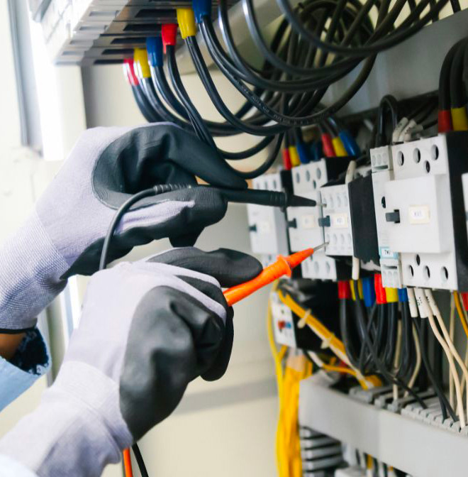 Un technicien en gants de protection effectue des ajustements dans un tableau électrique